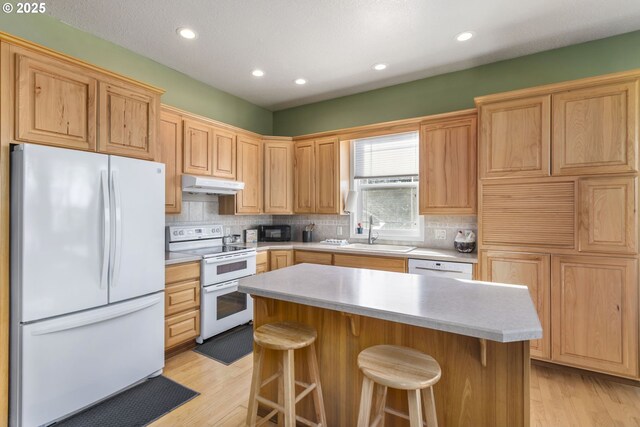 kitchen featuring decorative backsplash, a breakfast bar, white appliances, sink, and a center island