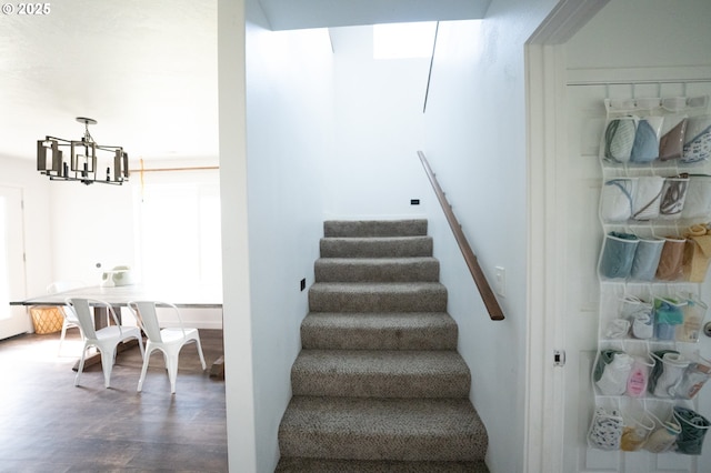 staircase with wood finished floors and an inviting chandelier
