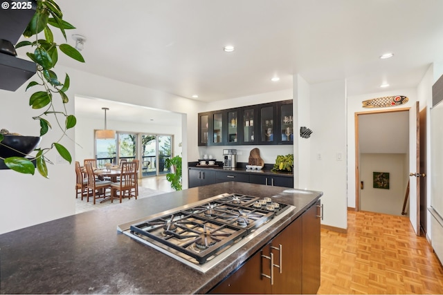kitchen with glass insert cabinets, dark countertops, hanging light fixtures, stainless steel gas stovetop, and recessed lighting