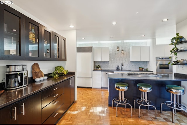 kitchen with white cabinetry, appliances with stainless steel finishes, dark countertops, and a breakfast bar
