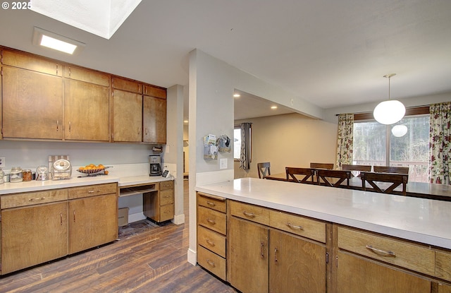 kitchen with light countertops, brown cabinets, dark wood-style floors, built in desk, and decorative light fixtures