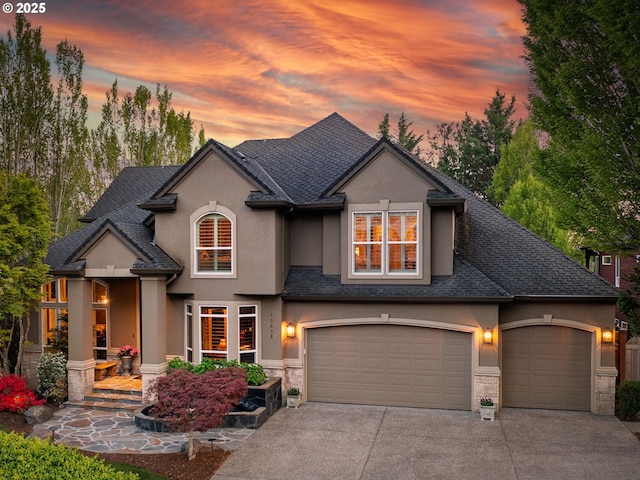 view of front of property with concrete driveway, stone siding, a shingled roof, an attached garage, and stucco siding