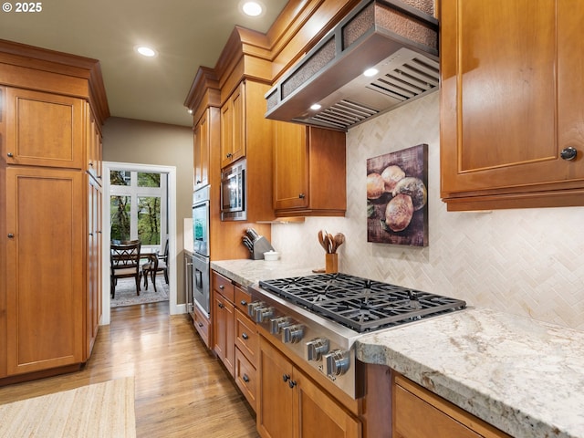 kitchen with brown cabinets, light wood-style flooring, tasteful backsplash, appliances with stainless steel finishes, and custom exhaust hood