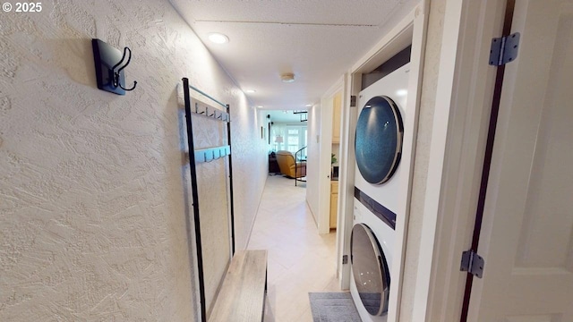 washroom with laundry area, stacked washer / drying machine, and a textured wall