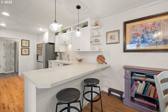kitchen featuring a breakfast bar, freestanding refrigerator, light wood-type flooring, light countertops, and white cabinets