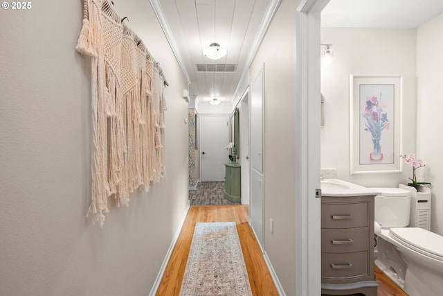 corridor with attic access, visible vents, baseboards, light wood-style floors, and ornamental molding