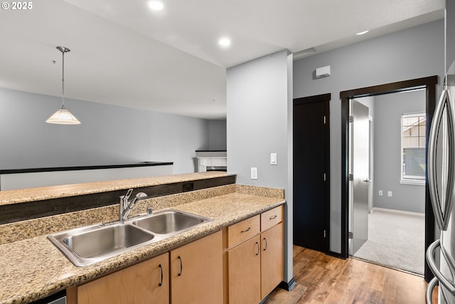kitchen featuring a sink, light brown cabinetry, light wood-style flooring, light countertops, and decorative light fixtures