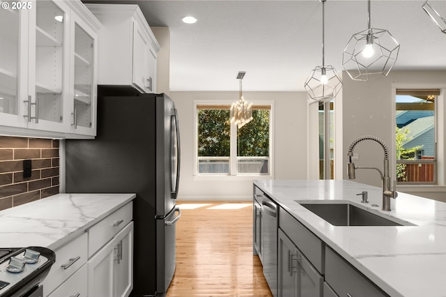 kitchen with a sink, decorative light fixtures, light wood-style flooring, backsplash, and light stone countertops
