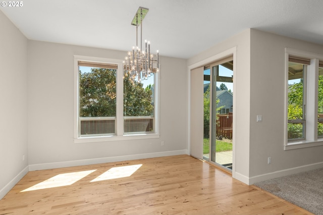 unfurnished dining area with an inviting chandelier, wood finished floors, baseboards, and a healthy amount of sunlight