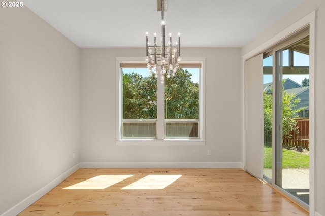 unfurnished dining area featuring light wood-type flooring, baseboards, a healthy amount of sunlight, and a notable chandelier