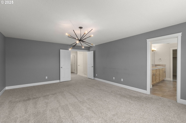 unfurnished bedroom featuring light colored carpet, an inviting chandelier, connected bathroom, and baseboards