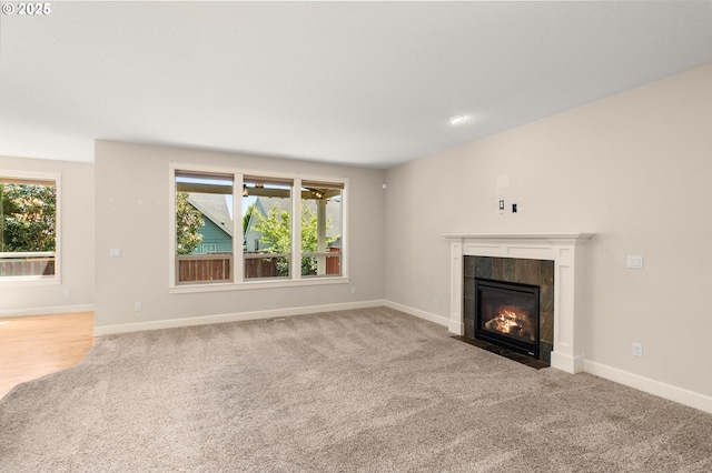 unfurnished living room with baseboards, a wealth of natural light, a tiled fireplace, and carpet floors
