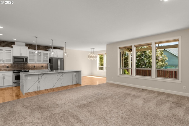 kitchen with white cabinetry, baseboards, stainless steel appliances, and an island with sink