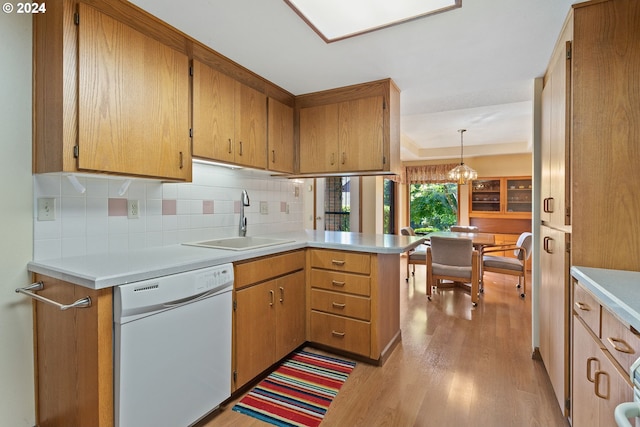 kitchen with a peninsula, white dishwasher, light countertops, light wood-type flooring, and a sink