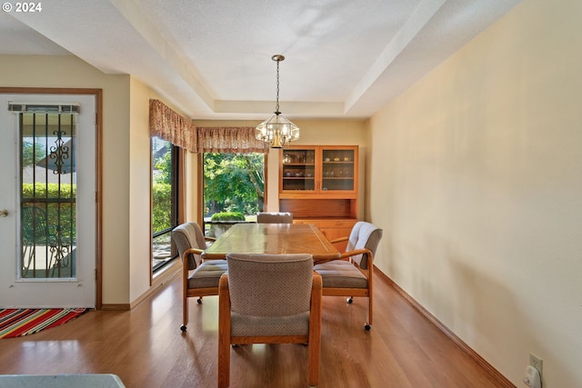 dining room with a tray ceiling, a notable chandelier, baseboards, and wood finished floors