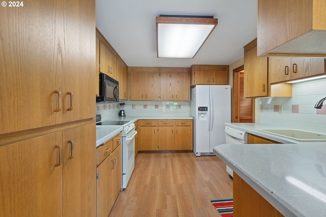 kitchen with white appliances, tasteful backsplash, light countertops, light wood-type flooring, and a sink