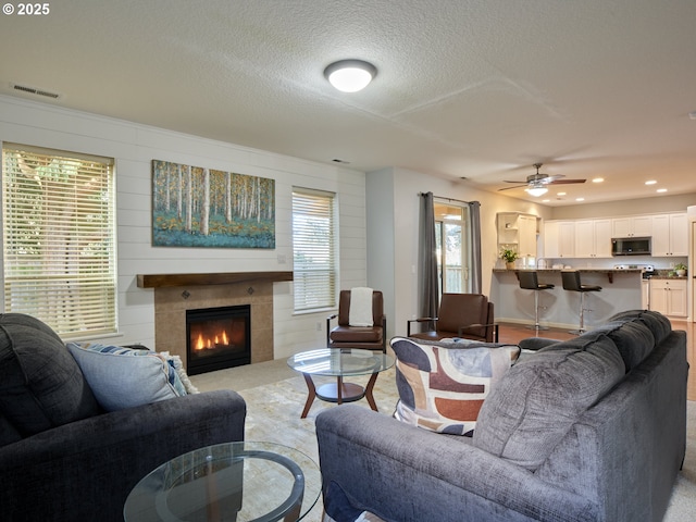 living room with a textured ceiling, a tiled fireplace, and ceiling fan