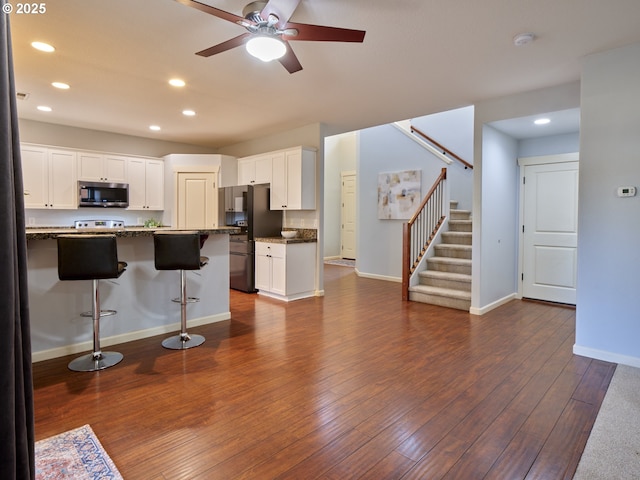 kitchen featuring white cabinetry, black fridge, ceiling fan, a breakfast bar, and dark wood-type flooring