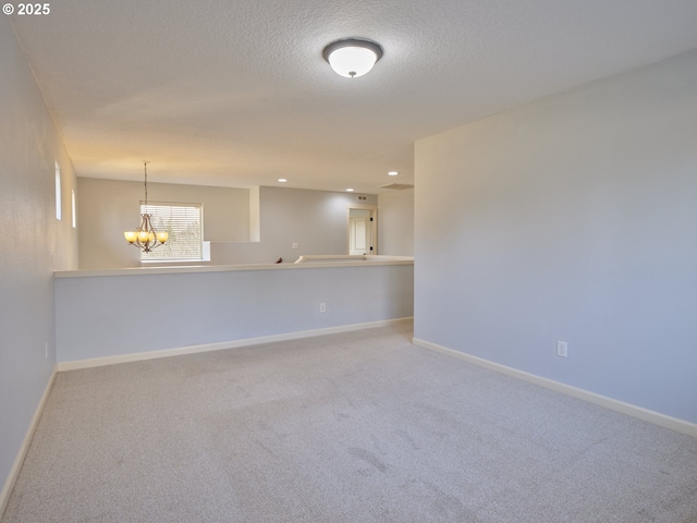 spare room featuring a textured ceiling, carpet floors, and a notable chandelier