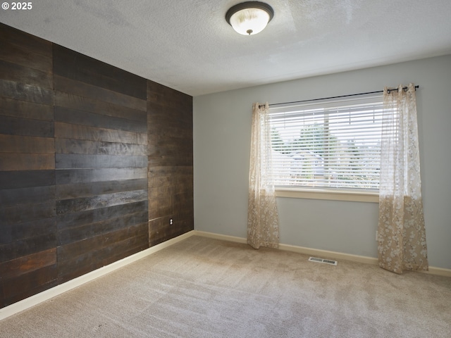 spare room featuring a textured ceiling, wood walls, and carpet