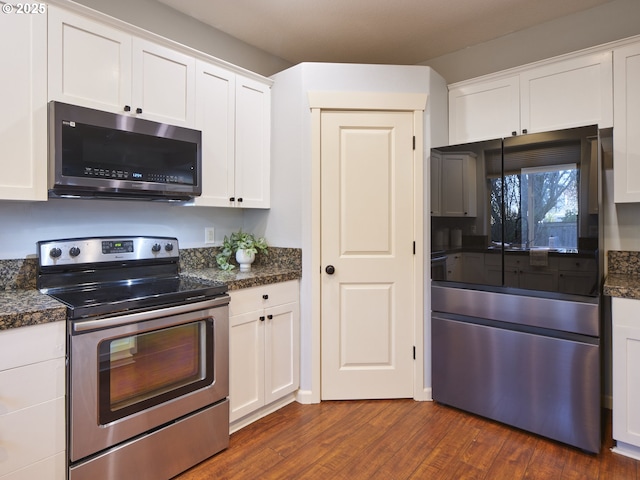 kitchen with appliances with stainless steel finishes, dark wood-type flooring, dark stone counters, and white cabinets