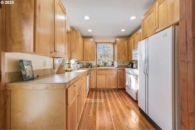 kitchen with tile countertops, sink, light brown cabinets, white appliances, and light hardwood / wood-style flooring