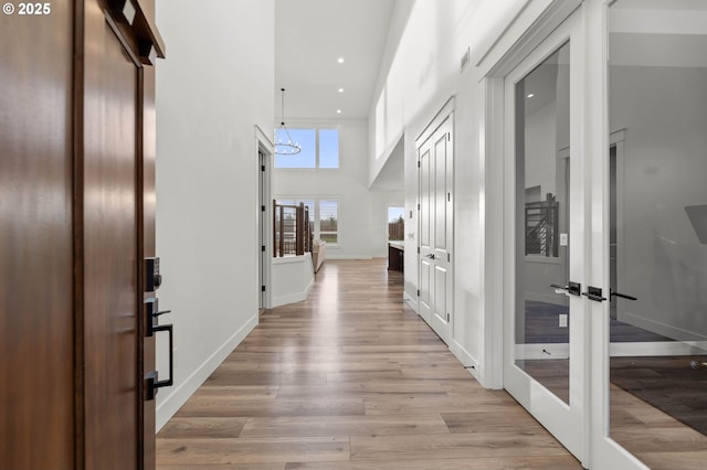 hallway with french doors, a high ceiling, and light wood-type flooring