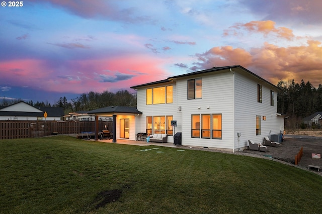 back house at dusk with central AC, a patio area, and a lawn