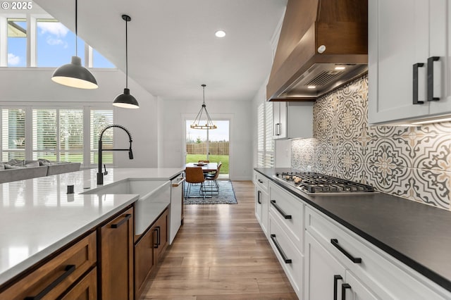 kitchen with sink, white cabinetry, pendant lighting, stainless steel appliances, and wall chimney range hood