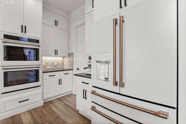 kitchen featuring backsplash, white appliances, light hardwood / wood-style flooring, and white cabinets