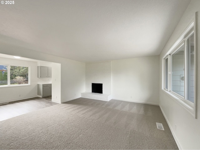 unfurnished living room with baseboards, light carpet, a brick fireplace, and visible vents
