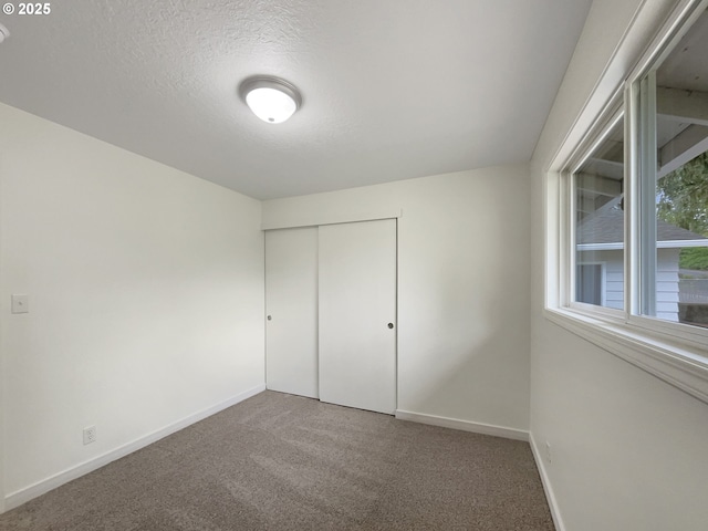 unfurnished bedroom featuring carpet floors, a textured ceiling, baseboards, and a closet
