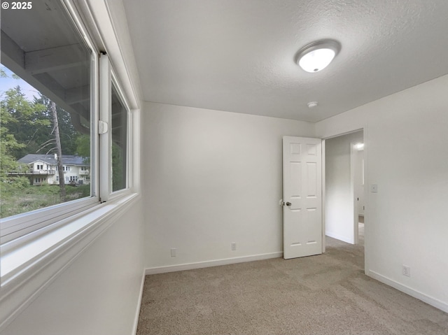 unfurnished room featuring baseboards, light carpet, and a textured ceiling