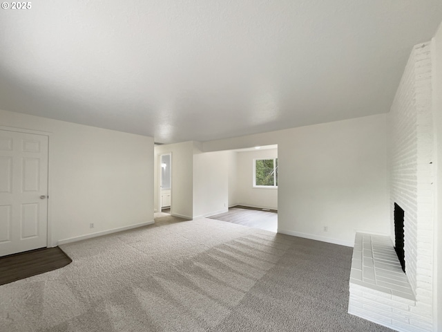 unfurnished living room with a brick fireplace, baseboards, and carpet