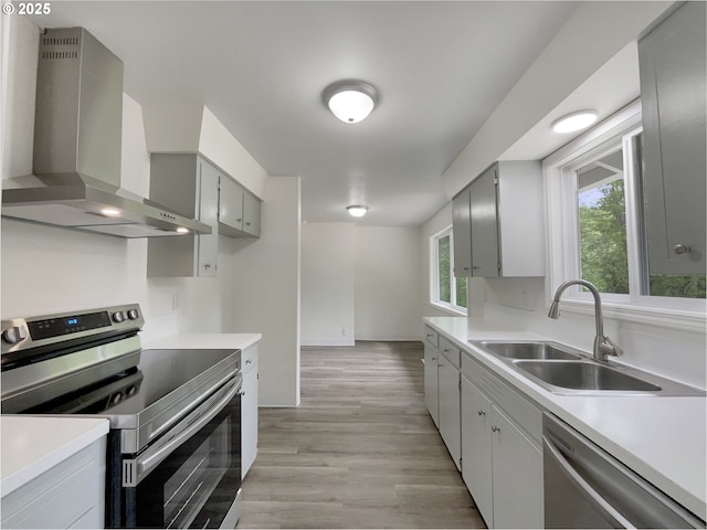 kitchen with wall chimney exhaust hood, a sink, light countertops, stainless steel appliances, and light wood-style flooring