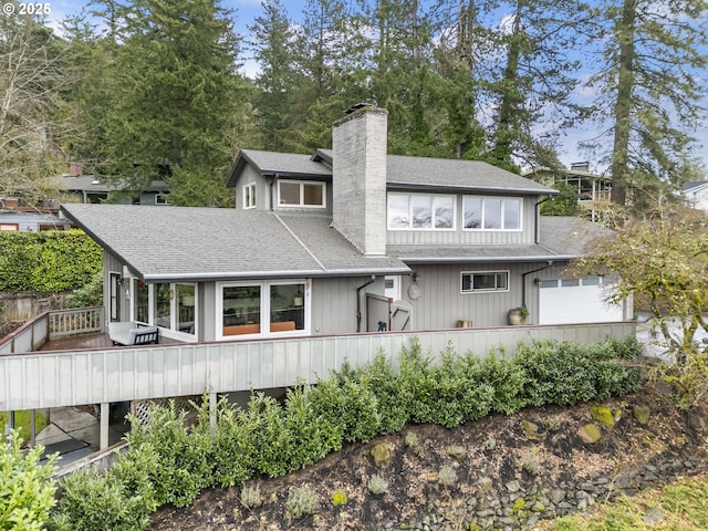 back of property featuring an attached garage, a shingled roof, and a chimney