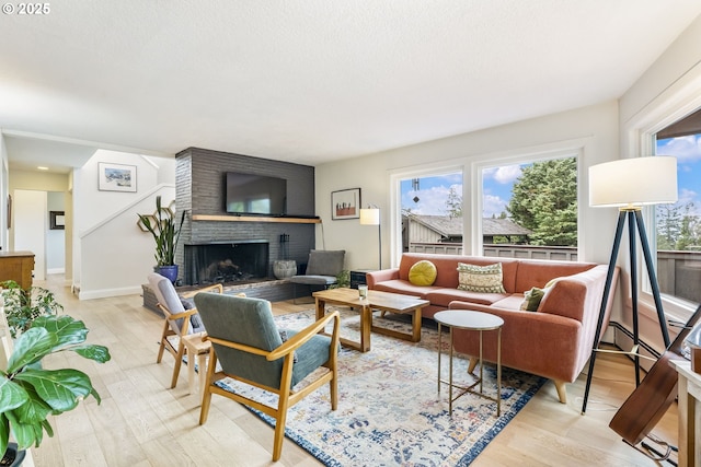 living area with a brick fireplace, baseboards, plenty of natural light, and light wood finished floors