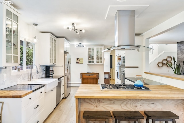 kitchen featuring island range hood, stainless steel appliances, wood counters, white cabinets, and decorative backsplash