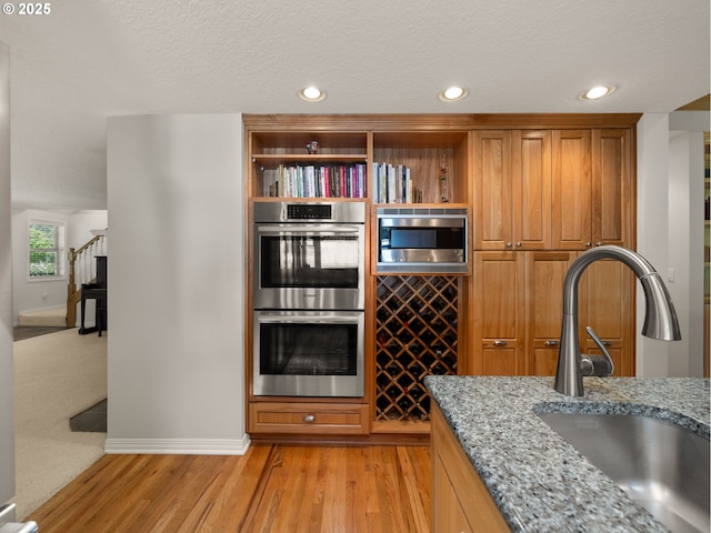 25210 E Arrah Wanna Blvd, Welches, OR 97067 - kitchen featuring a sink, appliances with stainless steel finishes, light wood-type flooring, light stone counters, and brown cabinetry