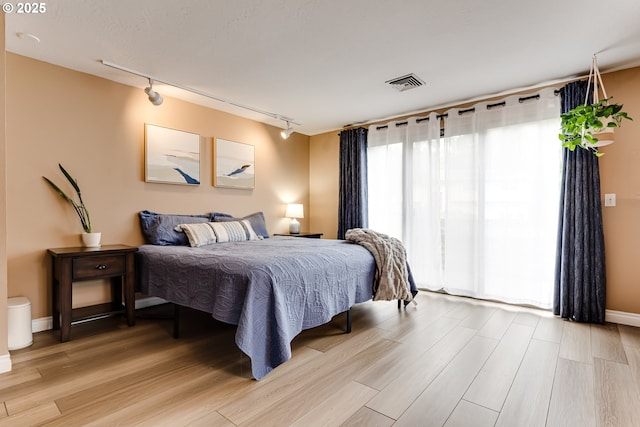 bedroom featuring track lighting, light wood finished floors, and baseboards
