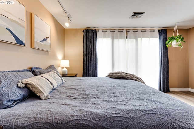 bedroom with multiple windows, wood finished floors, track lighting, and baseboards