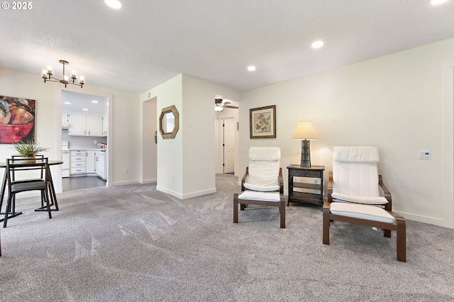 living area featuring light colored carpet, ceiling fan with notable chandelier, and a textured ceiling