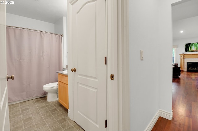 full bath with a fireplace, vanity, baseboards, toilet, and recessed lighting