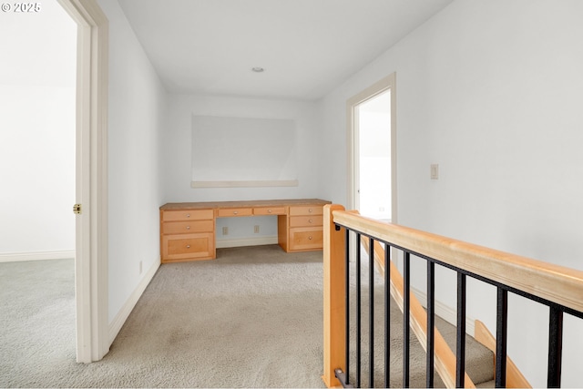 hallway featuring light colored carpet and baseboards