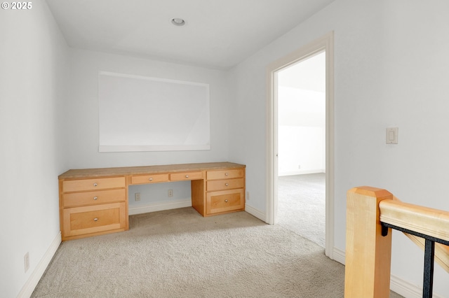 unfurnished office with built in study area, baseboards, and light colored carpet