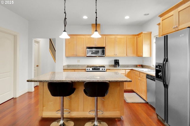 kitchen with a kitchen island, light brown cabinetry, wood finished floors, light stone counters, and stainless steel appliances