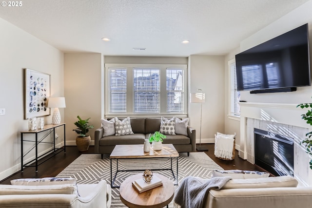 living room featuring a tile fireplace, a textured ceiling, and dark hardwood / wood-style floors