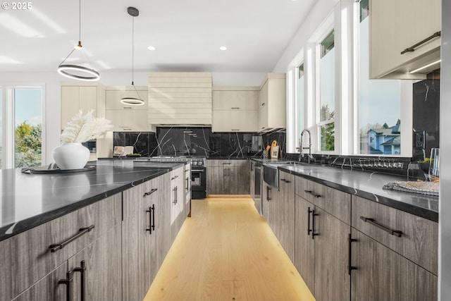 kitchen featuring sink, backsplash, dark stone counters, hanging light fixtures, and light hardwood / wood-style flooring