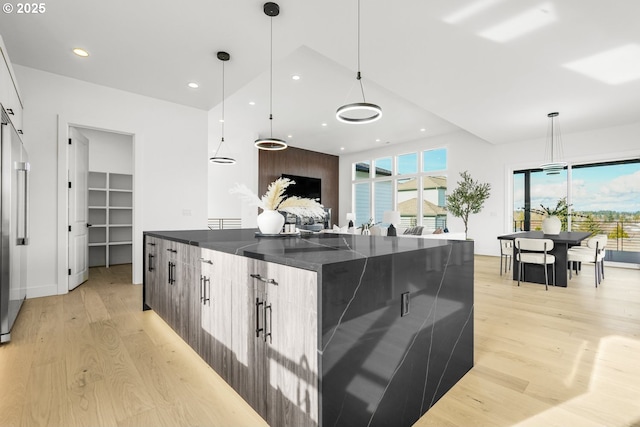 kitchen featuring dark stone counters, a kitchen island, hanging light fixtures, and light hardwood / wood-style flooring