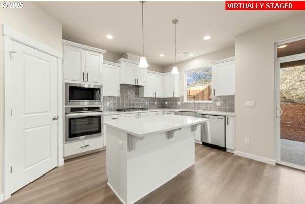 10587 SE Webelos Way, Happy Valley, OR 97086 - kitchen featuring appliances with stainless steel finishes, light wood-type flooring, backsplash, light countertops, and white cabinets